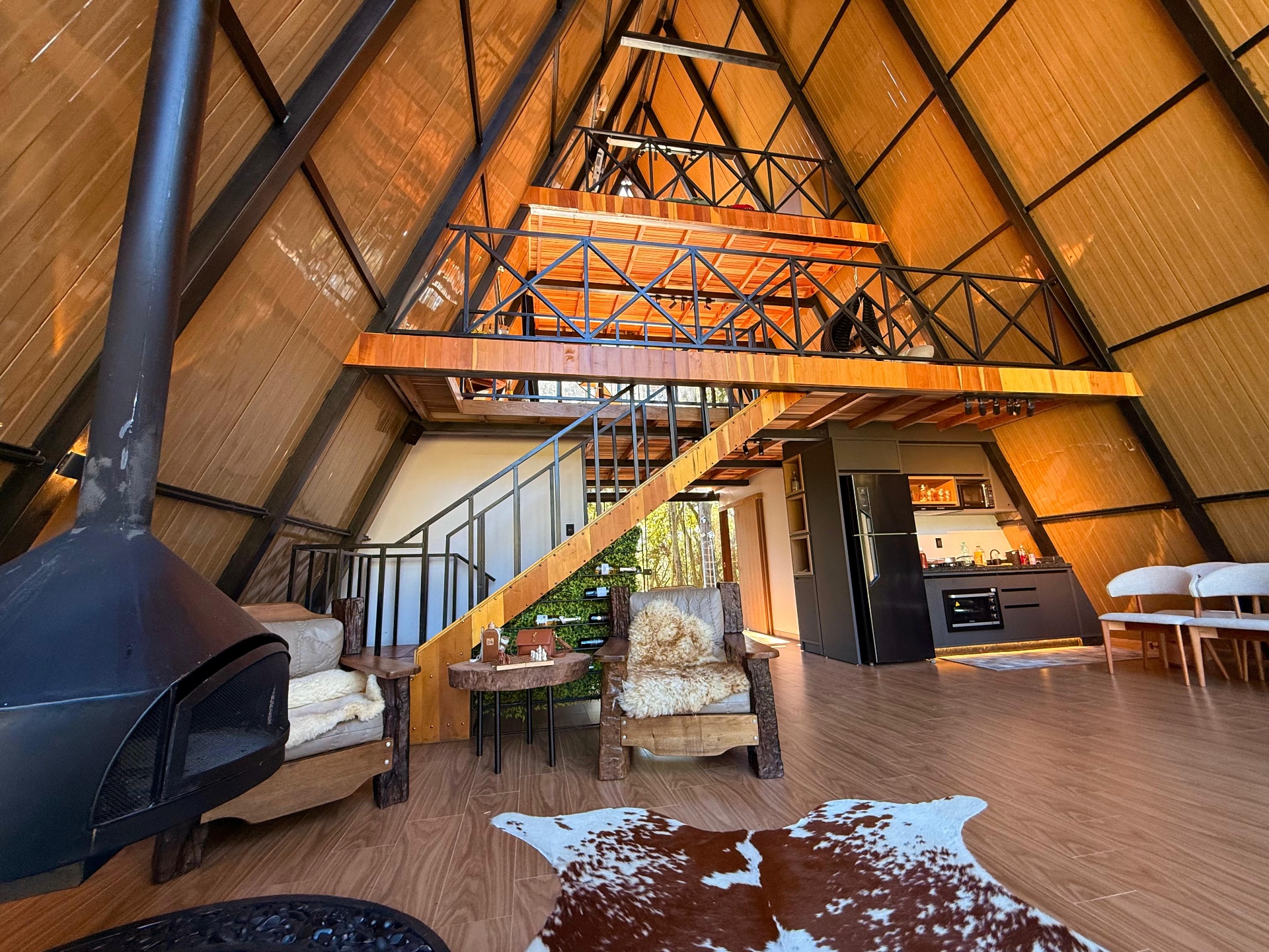 Sala aconchegante do chalé com lareira de pedra e vista para a floresta
